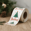 Rolka świątecznych naklejek na stole, na których widnieje ozdobiona choinka, gwiazdki oraz napis „Greatest Christmas Cheer Points”. W tle gałązki i szyszki.