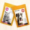 Dwa stojące żółte opakowania karmy dla zwierząt na jasnym tle. Lewy worek z wizerunkiem szarego kota i etykietą „Cat Food”, prawy worek z wizerunkiem psa o brązowo-białym umaszczeniu i etykietą „Dog Food”. Na obu opakowaniach widoczne logo „Hella – Pets we love” oraz okrągły znak „Holistic Wellness”. Poniżej na obu opakowaniach napis „100% pure goodness”