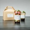 Brązowe pudełko oraz dwa plastikowe kubki z sałatką, oznaczone białymi etykietami z napisem „Avo & Quinoa Salad”. Opakowania stoją na szarym blacie.