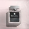 Kwadratowy flakon perfum z metalową zatyczką. Na etykiecie widnieje napis „BELUZZA FLORAL FRAGRANCE”. Flakon stoi na jasnoróżowym tle, cień pada na lewo.