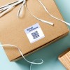 Kartonowe pudełko przewiązane białą wstążką, na wierzchu kwadratowa biała etykieta z napisem „Splash Creations” i kodem QR, pełniąca funkcję etykiety prezentowej lub firmowej