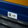 Zbliżenie na białą etykietę z kodem QR i oznaczeniem „L10”, naklejoną na niebieskim regale magazynowym.