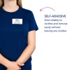 Obraz przedstawia osobę ubraną w ciemnoniebieską koszulę z identyfikatorem, na którym widnieje napis „B. Carlos, Dyrektor ds. Marketingu”. Dodatkowo jest tekst opisujący funkcję samoprzylepną identyfikatora, który stwierdza, że przykleja się niezawodnie do ubrań i łatwo usuwa bez pozostawiania śladów.