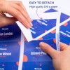 Obraz przedstawia dłonie odłączające sekcję z wysokiej jakości zadrukowanego papieru z widocznymi nazwiskami i rolami. Tło ma żywy design z niebieskimi i czerwonymi elementami.