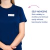 Obraz przedstawia osobę ubraną w granatową koszulę z plakietką z napisem 'B. Carlos, Dyrektor Marketingu.' Jest również opis, który stwierdza, że plakietka jest samoprzylepna i może niezawodnie przyklejać się do ubrań, nie pozostawiając śladów.