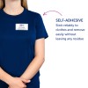 Obraz przedstawia osobę ubraną w granatową koszulkę z samoprzylepną plakietką z imieniem, na której widnieje napis „B. Carlos, Dyrektor ds. Marketingu.” Obok znajduje się opis podkreślający samoprzylepne właściwości plakietki, zaznaczający jej niezawodność i łatwość usunięcia bez pozostawiania śladów.