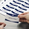 Obraz przedstawia rękę trzymającą identyfikator z nazwiskiem 'Catherin Molton', otoczony przez wydrukowany arkusz z wieloma identyfikatorami w tle.