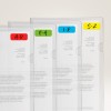 Obraz przedstawia serię przezroczystych plastikowych folderów ustawionych obok siebie, każdy oznaczony etykietą wskazującą na sekcje zorganizowane według zakresów liter: A-D w kolorze czerwonym, E-H w zielonym, I-R w niebieskim i S-Z w żółtym. Zawierają one wydrukowane dokumenty, choć tekst jest częściowo zasłonięty.