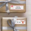 Obraz przedstawia dwa pięknie zapakowane prezenty w złotym papierze, każdy ozdobiony srebrnymi wstążkami. Jeden prezent ma metkę z napisem „Fröhliche Weihnachten!” i ilustracją Świętego Mikołaja, a drugi jest oznaczony „Für Lina” z ilustracją renifera.